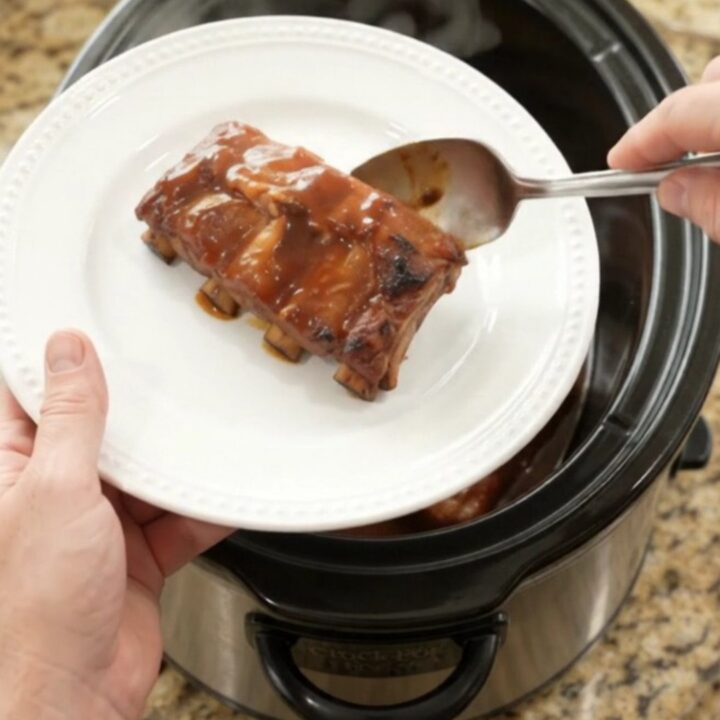 Slow-cooker pineapple BBQ baby back ribs in a black crockpot with pineapple rings and sauce
