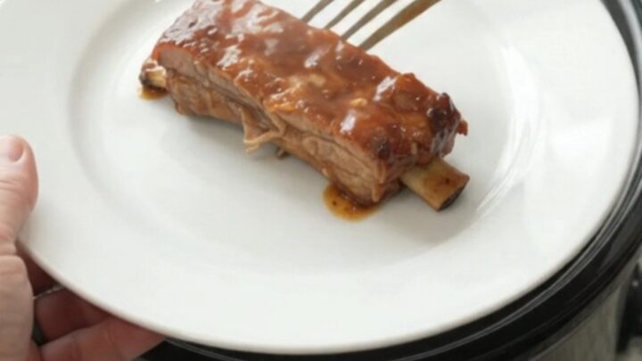 Slow-cooker baby back ribs glazed with peach BBQ sauce, garnished with sliced peaches.