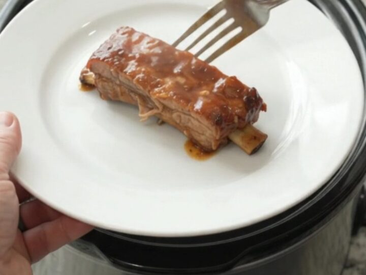 Slow-cooker baby back ribs glazed with peach BBQ sauce, garnished with sliced peaches.