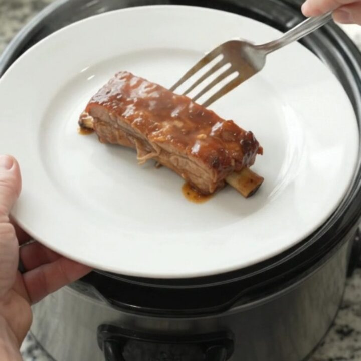 Slow-cooker baby back ribs glazed with peach BBQ sauce, garnished with sliced peaches.