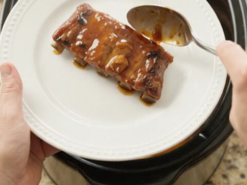 Slow cooker ribs with peaches and bourbon glaze, garnished with fresh herbs on a white plate