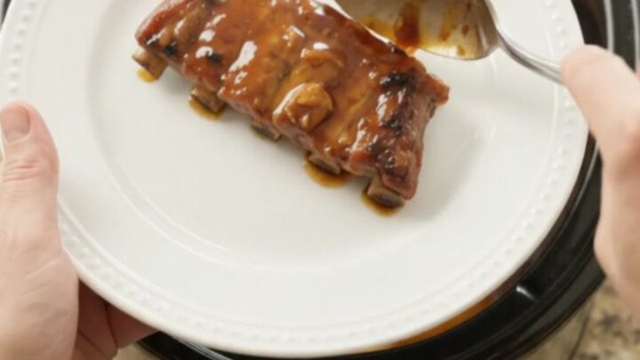 Slow cooker ribs with peaches and bourbon glaze, garnished with fresh herbs on a white plate
