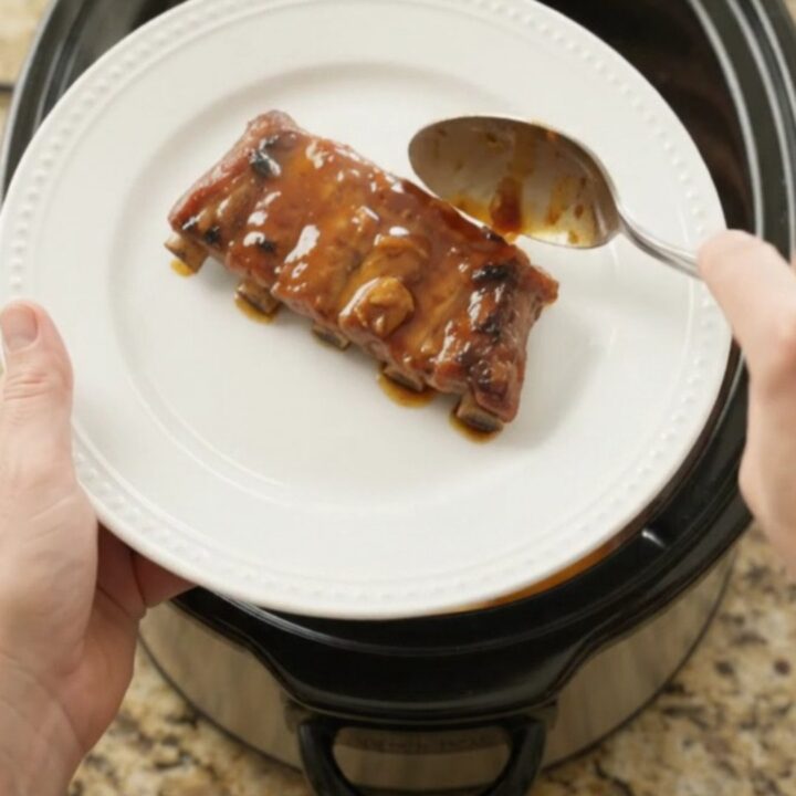 Slow cooker ribs with peaches and bourbon glaze, garnished with fresh herbs on a white plate