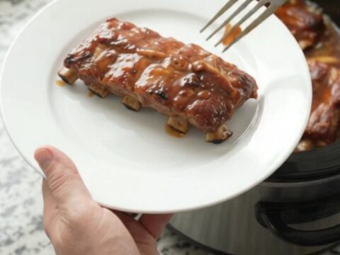 Slow-cooker baby back ribs glazed with smoky chipotle honey hickory sauce, served on a white plate.
