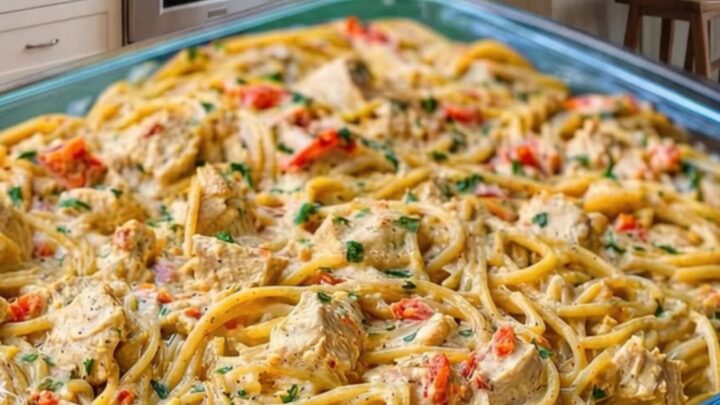 A glass baking dish filled with creamy chicken spaghetti topped with melted golden cheese and fresh parsley garnish.