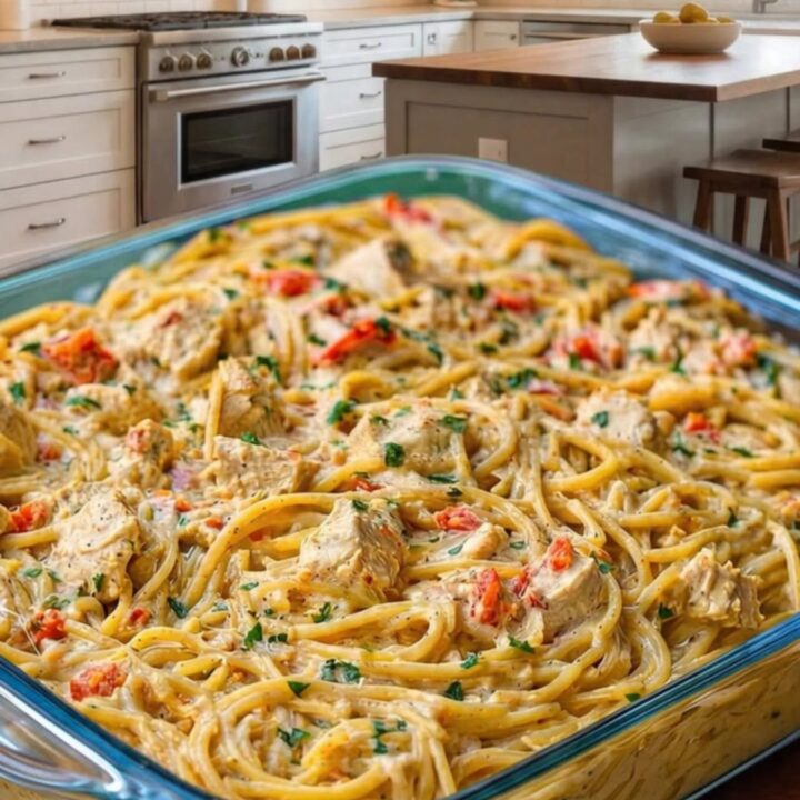 A glass baking dish filled with creamy chicken spaghetti topped with melted golden cheese and fresh parsley garnish.