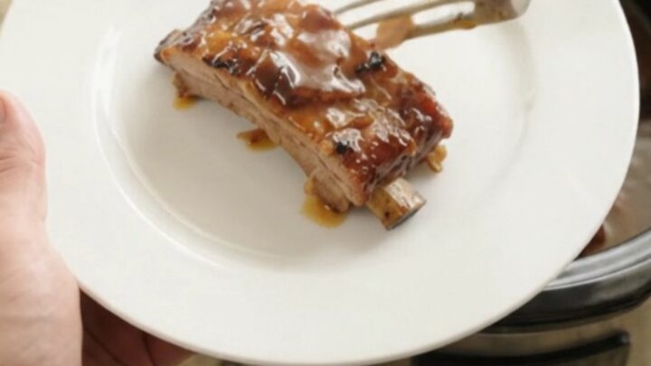 Slow cooker full of glazed baby back ribs in bubbling sauce
