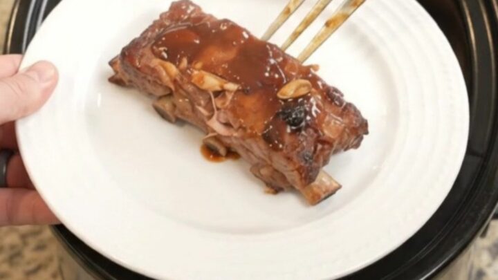 Slow cooker baby back ribs glazed with BBQ sauce, garnished with rosemary