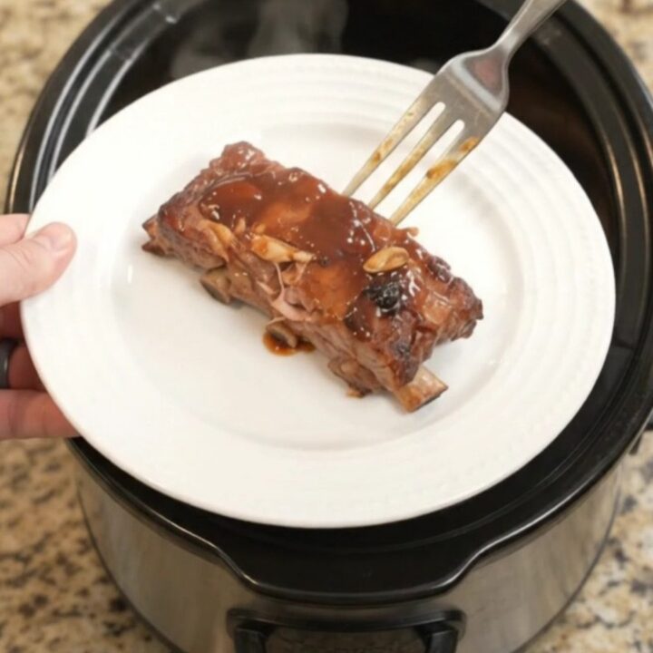 Slow cooker baby back ribs glazed with BBQ sauce, garnished with rosemary