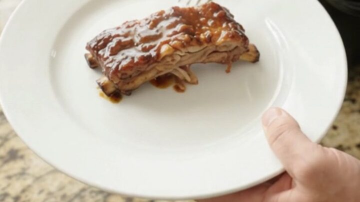Slow cooker molasses garlic baby back ribs, glistening with dark sauce and topped with rosemary and garlic confit.