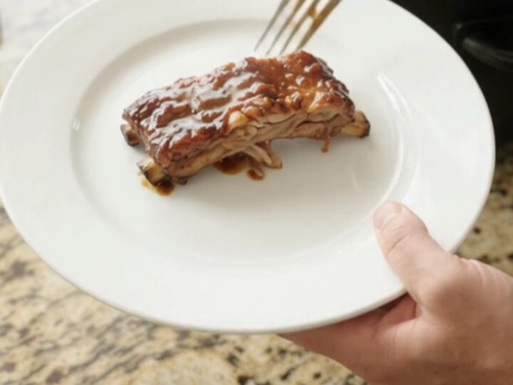 Slow cooker molasses garlic baby back ribs, glistening with dark sauce and topped with rosemary and garlic confit.