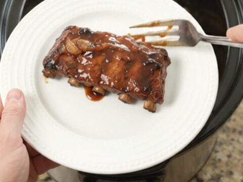 Slow cooker baby back ribs glistening with molasses garlic sauce and caramelized onions