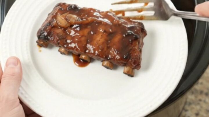 Slow cooker baby back ribs glistening with molasses garlic sauce and caramelized onions