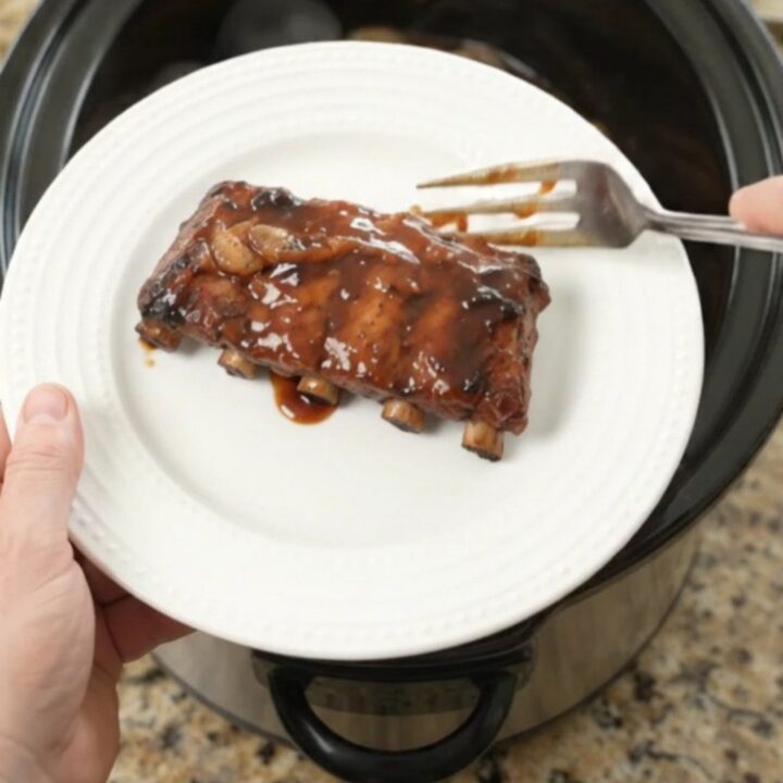 Slow cooker baby back ribs glistening with molasses garlic sauce and caramelized onions