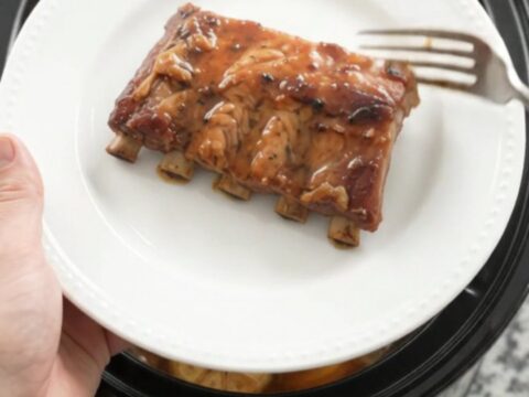 Tender baby back ribs coated in glossy maple bourbon BBQ sauce in a slow cooker