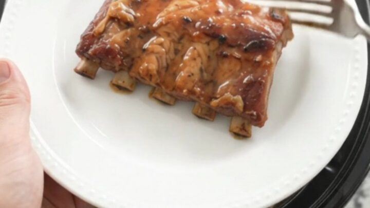 Tender baby back ribs coated in glossy maple bourbon BBQ sauce in a slow cooker