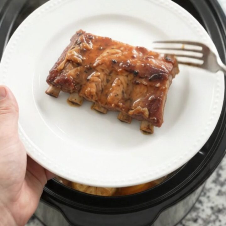 Tender baby back ribs coated in glossy maple bourbon BBQ sauce in a slow cooker