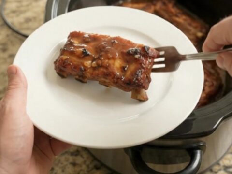 A slow cooker filled with glistening baby back ribs in a rich honey hickory BBQ sauce, steam rising.