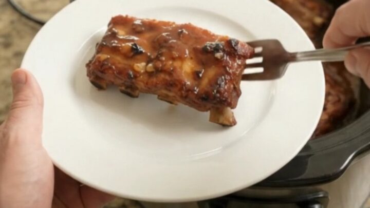 A slow cooker filled with glistening baby back ribs in a rich honey hickory BBQ sauce, steam rising.