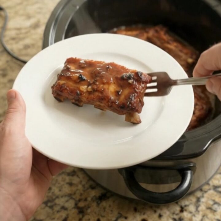 A slow cooker filled with glistening baby back ribs in a rich honey hickory BBQ sauce, steam rising.