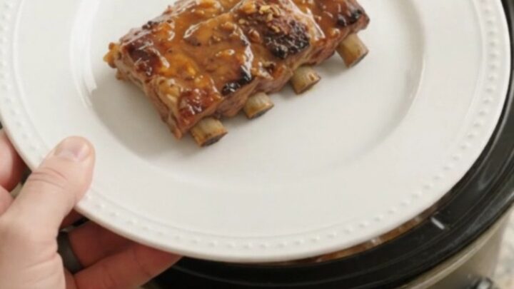 Slow-cooker baby back ribs glazed with maple bourbon sauce, garnished with fresh parsley on a white plate.