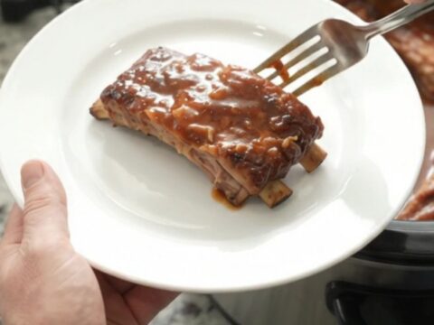 Slow cooker full of glazed baby back ribs with caramelized onions and BBQ sauce.