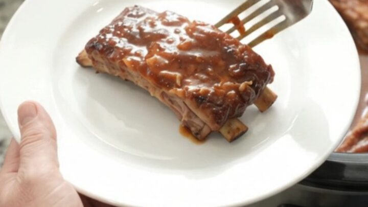 Slow cooker full of glazed baby back ribs with caramelized onions and BBQ sauce.