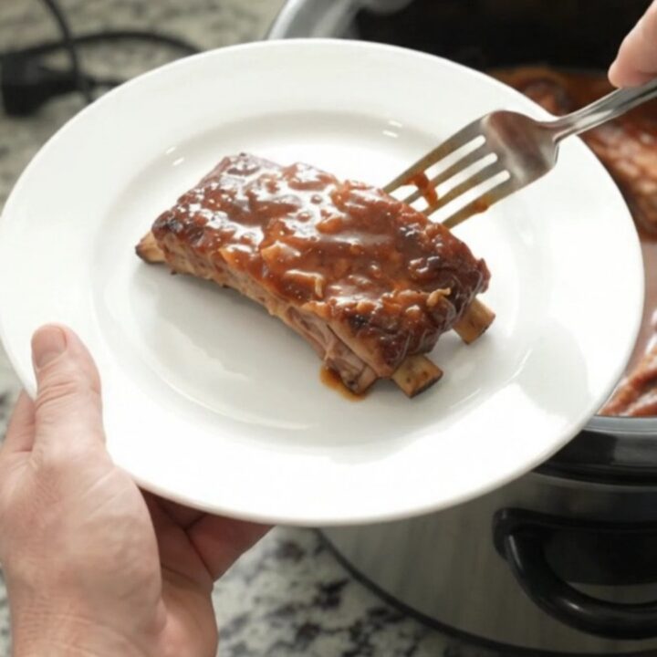 Slow cooker full of glazed baby back ribs with caramelized onions and BBQ sauce.