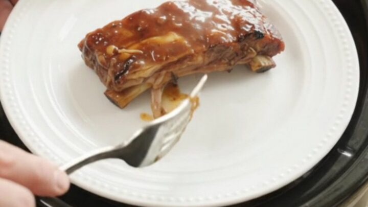 Slow cooker root beer BBQ baby back ribs glistening with sauce, garnished with caramelized onions