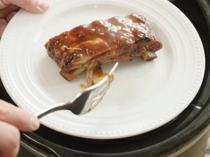 Slow cooker root beer BBQ baby back ribs glistening with sauce, garnished with caramelized onions
