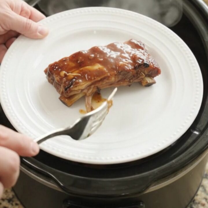 Slow cooker root beer BBQ baby back ribs glistening with sauce, garnished with caramelized onions