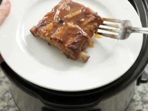 Slow cooker full of glazed root beer baby back ribs topped with caramelized onions
