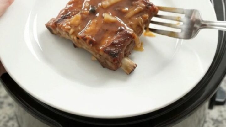 Slow cooker full of glazed root beer baby back ribs topped with caramelized onions
