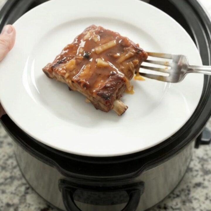 Slow cooker full of glazed root beer baby back ribs topped with caramelized onions