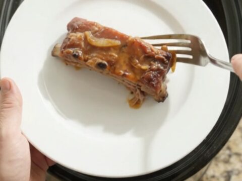 Baby back ribs in slow cooker with bubbling sauce and onions