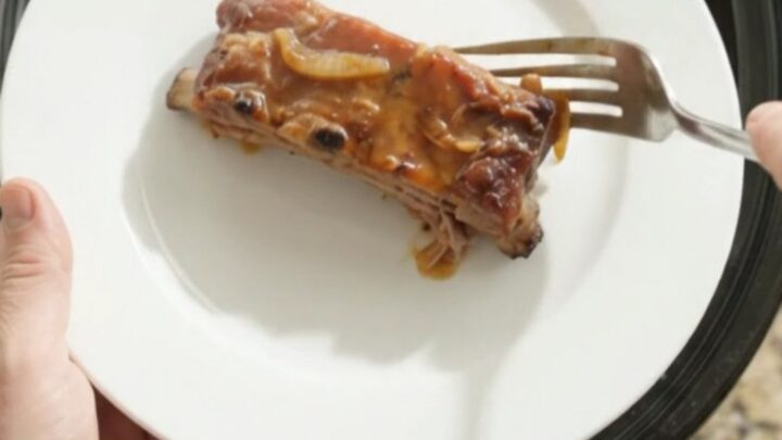 Baby back ribs in slow cooker with bubbling sauce and onions
