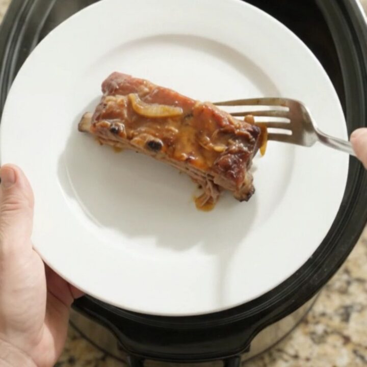Baby back ribs in slow cooker with bubbling sauce and onions