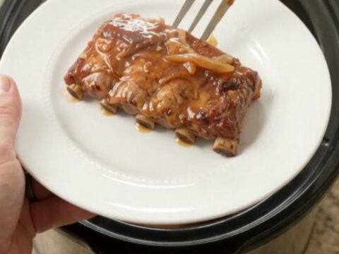 Pull-apart brown sugar maple bourbon spare ribs in a slow cooker with caramelized onions and glossy sauce.