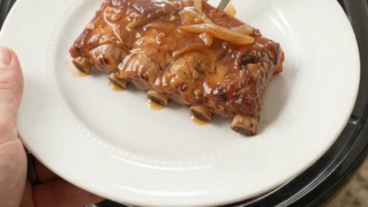 Pull-apart brown sugar maple bourbon spare ribs in a slow cooker with caramelized onions and glossy sauce.