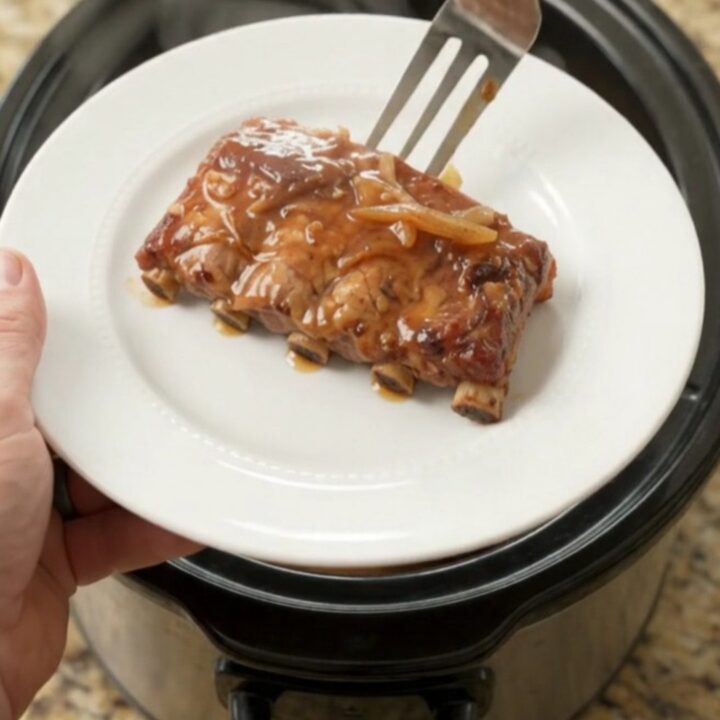 Pull-apart brown sugar maple bourbon spare ribs in a slow cooker with caramelized onions and glossy sauce.