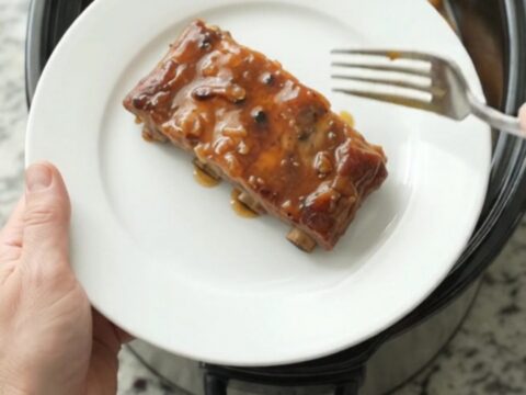 Slow cooker spare ribs glazed with maple bourbon BBQ sauce, topped with braised apple slices
