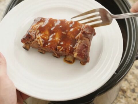 Glossy slow-cooked spare ribs in thick BBQ sauce with caramelized pineapple rings in a Crockpot