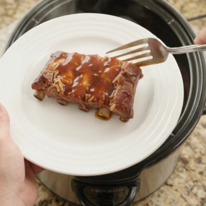 Glossy slow-cooked spare ribs in thick BBQ sauce with caramelized pineapple rings in a Crockpot