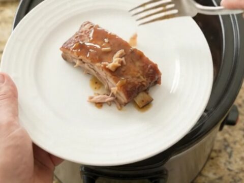 Slow cooker spare ribs glazed with honey-hickory barbecue sauce and peaches, lifted with a fork.