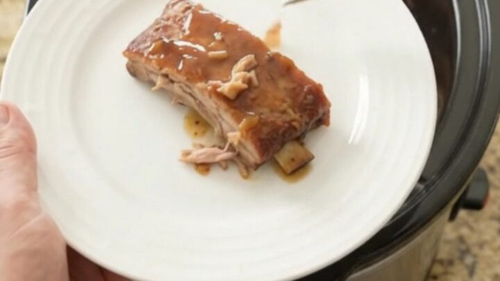 Slow cooker spare ribs glazed with honey-hickory barbecue sauce and peaches, lifted with a fork.
