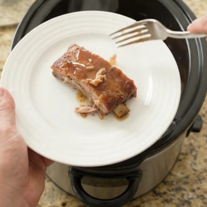 Slow cooker spare ribs glazed with honey-hickory barbecue sauce and peaches, lifted with a fork.