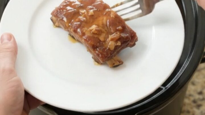 Slow-cooker spare ribs with pineapple rings in a glossy maple bourbon BBQ sauce, shown in the slow cooker.