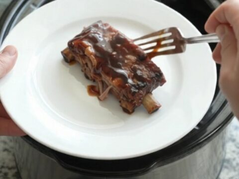Glossy cherry cola molasses spare ribs in a slow cooker, garnished with cherries