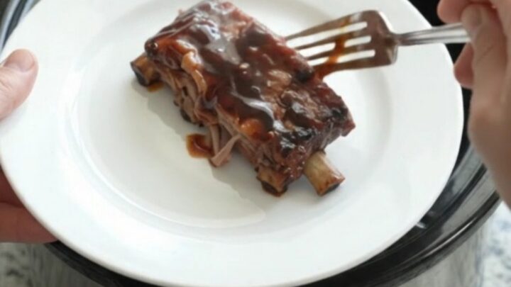 Glossy cherry cola molasses spare ribs in a slow cooker, garnished with cherries