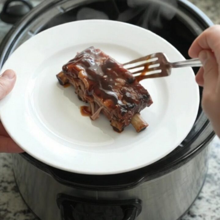 Glossy cherry cola molasses spare ribs in a slow cooker, garnished with cherries
